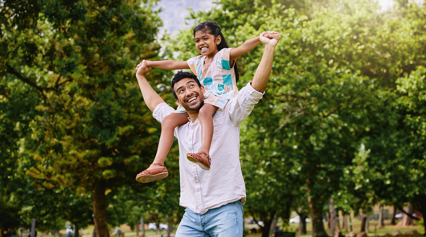 father carrying daughter on his shoulders, both laughing in fondness
